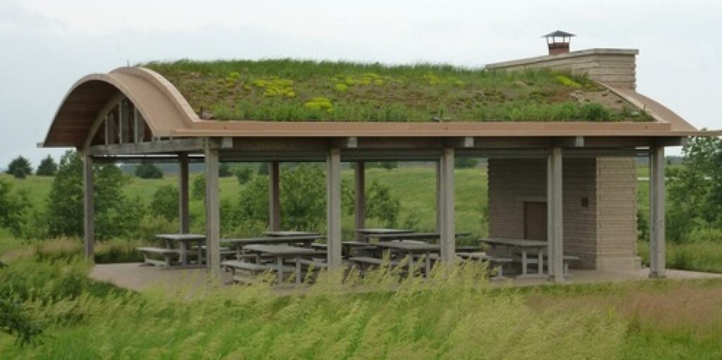View of the grass-covered pavilion and picnic tables at Brenton Arboretum, nestled among the trees and flowers, offering a serene and picturesque spot for visitors to relax and enjoy the natural surroundings.