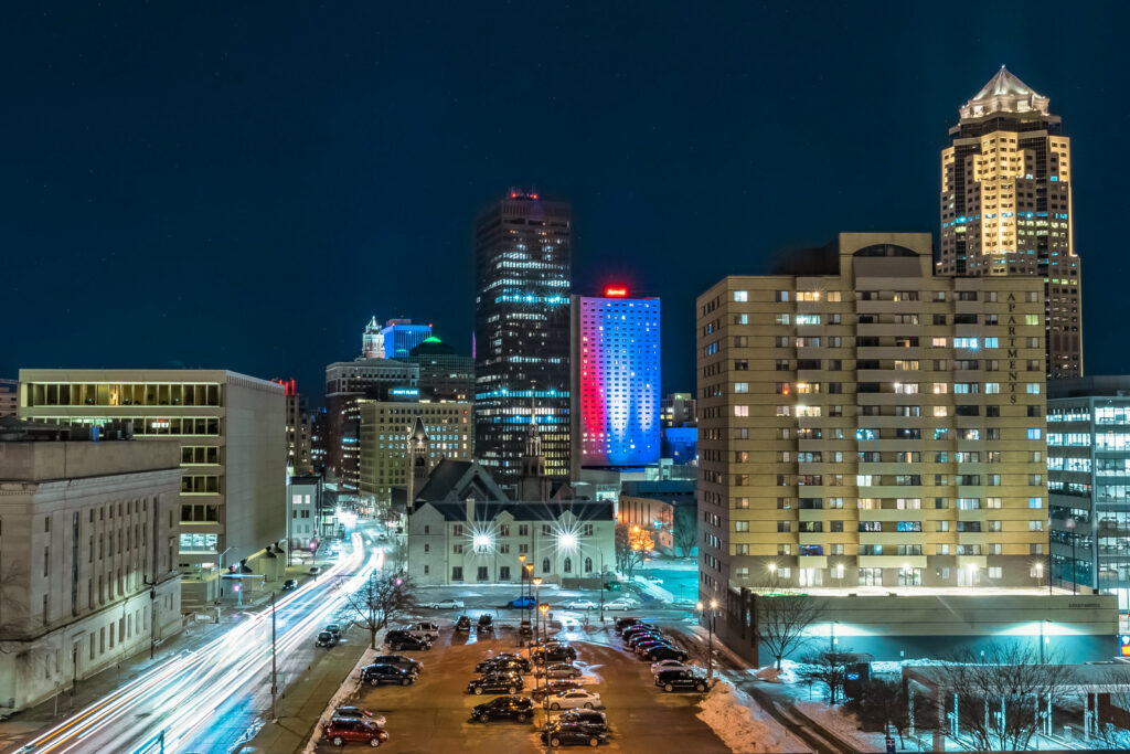 Vibrant night view of the Des Moines skyline, with colorful streaks of car headlights creating a dynamic and energetic atmosphere, showcasing the urban charm and excitement of the city.