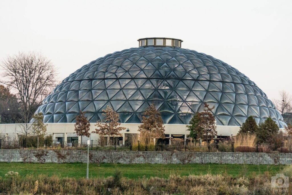 An impressive photo of the Greater Des Moines Botanical Garden building, featuring modern architecture with large glass windows that reflect the surrounding landscape, harmoniously blending the structure with the natural beauty of the gardens.