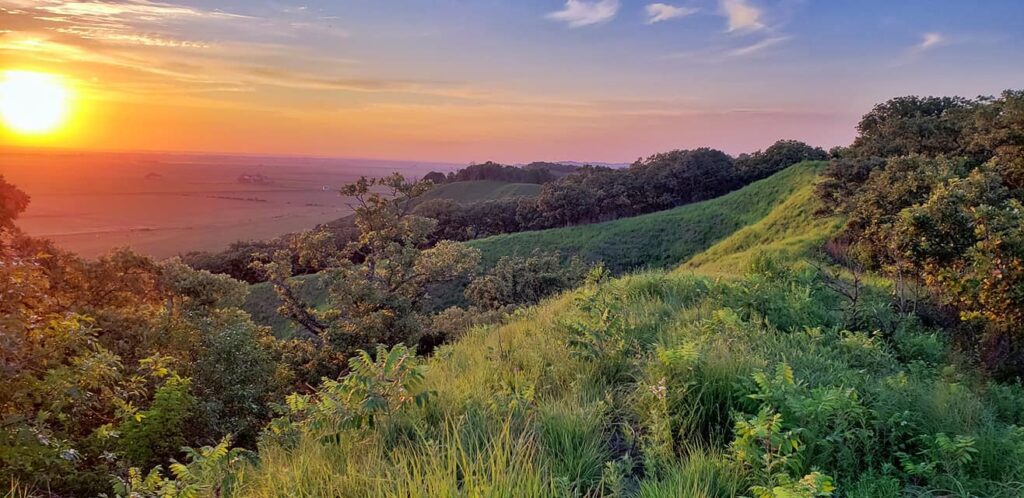 A mesmerizing photo of the Loess Hills at sunset, with the rolling hills and unique land formations bathed in warm, golden light, casting long shadows and creating a serene, otherworldly atmosphere.