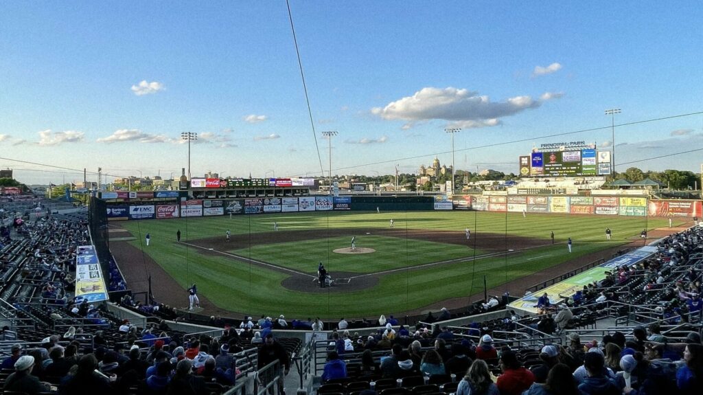 A lively photo of Principal Park, home of the Iowa Cubs, showcasing the well-maintained baseball field with bright green grass, fans filling the stands, and the Des Moines skyline in the background, capturing the excitement and community spirit of a game day."