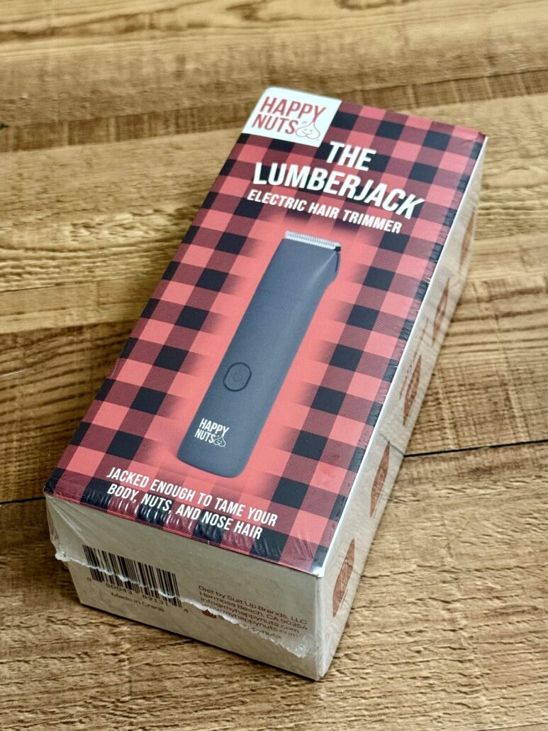 Retail box of the Happy Nuts Lumberjack Electric Hair Trimmer with bold plaid design and slogan: 'Jacked enough to tame your body, nuts, and nose hair.'