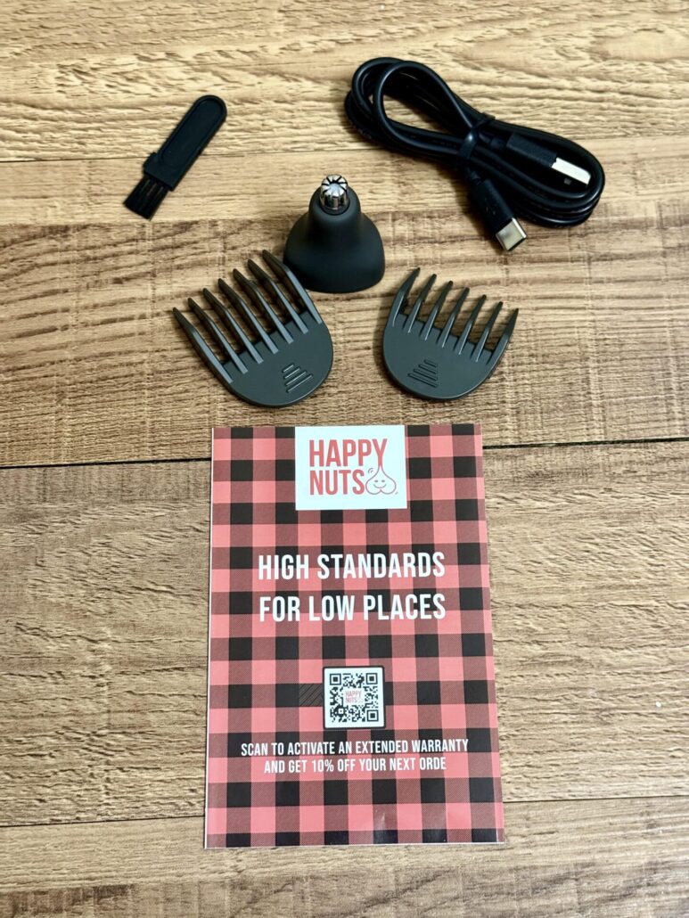 Happy Nuts Lumberjack trimmer accessories including two guide combs, a nose trimmer head, cleaning brush, USB-C charging cable, and warranty card on a wooden surface.